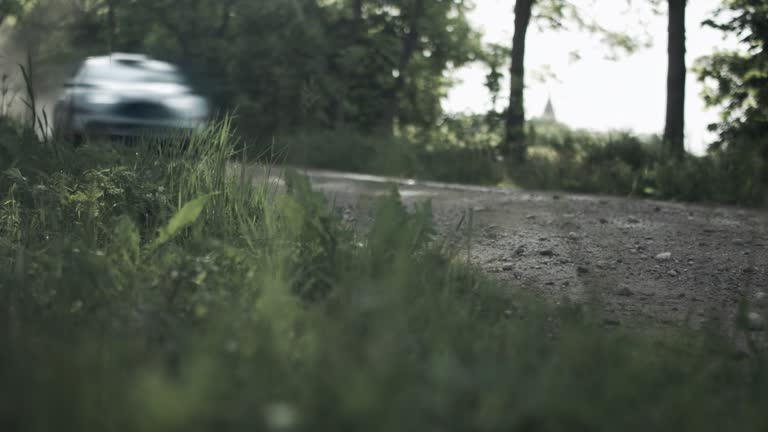 Low angle view sports car driving through the forest dirt road towards camera