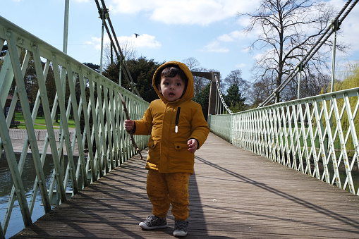 Cute Asian Pakistani Baby Ahmed Mustafain Haider is Enjoying The Beautiful Sunny and Cold Day at Wardown Public Park of Luton Town of England UK. The Baby is Wearing Yellow Trouser with Bright Yellow Hoody Jacket. Low Angle