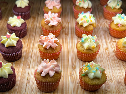 Stock photo showing close-up view of bakery wooden shelf display of individual cupcakes in paper cake cases available for purchasing.