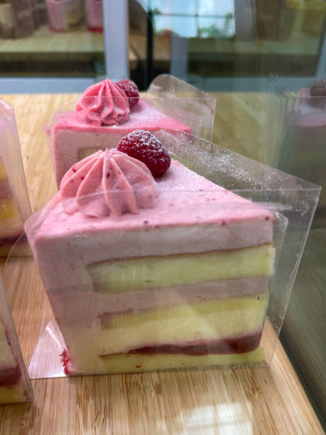 istock Close-up image of individual lemon and raspberry cake slice encased in clear plastic, bakery display of lemon sponge layers separated by raspberry buttercream, piped icing rosette, focus on foreground 1479995401