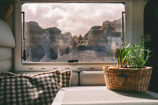 One woman sitting on the rocks view from inside modern camper van through the window. Concept of nomad lifestyle people and scenic travel destination. Alternative house and life. living off grid