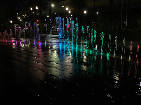 Stock photo showing pavement fountains in the middle of a city centre shopping plaza, where the sparkling jets of water come up through the paving slabs and drain away at the edge of the stones.