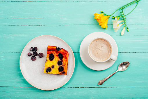 A cup of coffee and blueberry cake, yellow freesia flower on turquoise wooden table. Top view, flat lay.