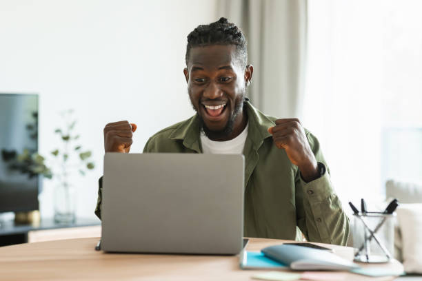 istock Overjoyed black male entrepreneur using laptop smiling and gesturing yes, sitting at workplace at home office 1480006725