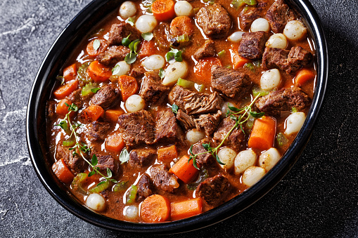 boneless beef short ribs stew with carrots and pearl onions in black bowl on concrete table, close-up