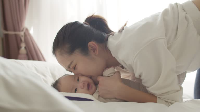 Happy young Asian mother playing with baby in bed.