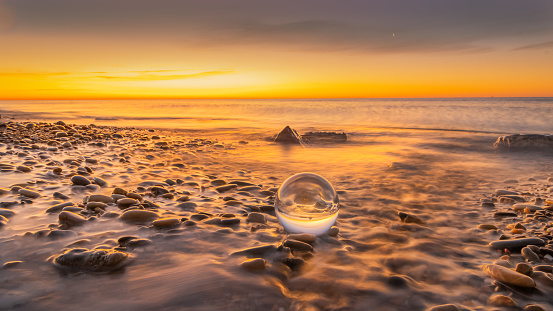 Crystal ball on pebbles of a beach at sunrise.