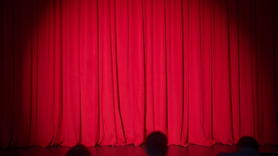 Red theater curtain with people sitting on seats in silhouette