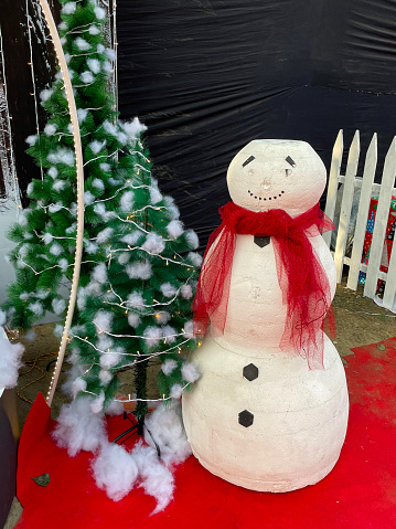 Stock photo showing close-up view of artificial Christmas tree covered in with cotton wool snowballs, with model snowman, as part of a festive public seasonal display at a shopping mall.