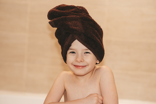 Joyful child in the bathroom with a towel on his head. Children hygiene.