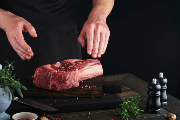 istock Chef cutting steak beef. Mans hands hold raw steak Tomahawk on rustic wooden cutting board on black background. Cooking, recipes and eating concept. Selective focus. 1480021399