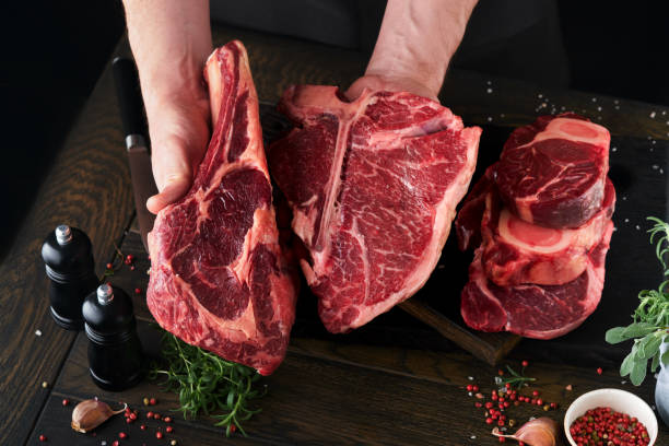 istock Chef cutting steak beef. Mans hands hold raw steak Tomahawk on rustic wooden cutting board on black background. Cooking, recipes and eating concept. Selective focus. 1480021775