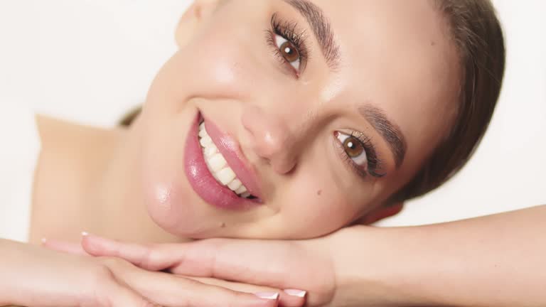 Fit European female beauty model in white crop top puts her head on her hand lying and looking at the camera on white background. Skin protection concept