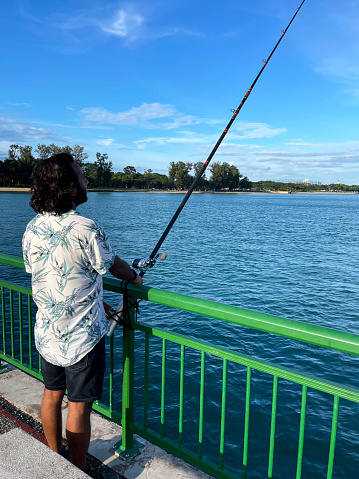 Stock photo showing close-up view of Bedok Jetty green railings with a fishing pole bound to top of railings, East Coast Park, Singapore.