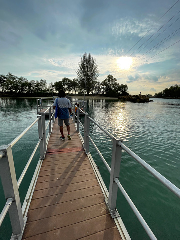 Stock photo showing a wooden plank pedestrian walkway and handrails of a boardwalk. This crossing enables walkers to travel over some water before reaching an island.