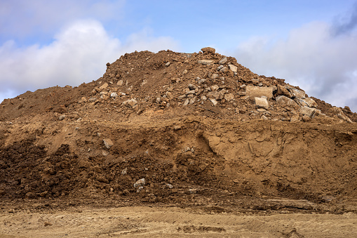 Excavated mounds of sand and concrete rubble are piled together against wheel traces against the sky as a backdrop to prepare materials for filling and repairing roads in rural Thailand during the dry season.
