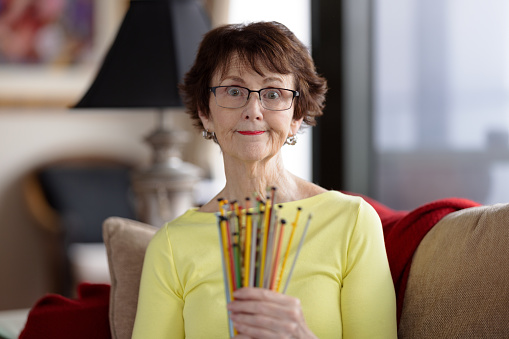 Confused senior woman at home holding a bunch of knitting needles.
