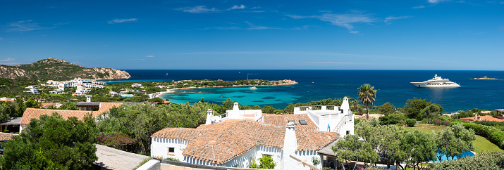 This stunning panorama captures the beauty of Porto Cervo village, located in the heart of the picturesque Sardinian coastline. The photo features the traditional terracotta tiles rooftops of the elegant villas, complemented by the luxurious yachts anchored in the crystal-clear waters. The surrounding beaches offer a pristine and serene atmosphere, showcasing the natural beauty of the island's landscape. From the vibrant hues of the sea to the lush greenery of the surrounding hills, this photo is a true testament to the breathtaking sights and experiences that Porto Cervo has to offer.
