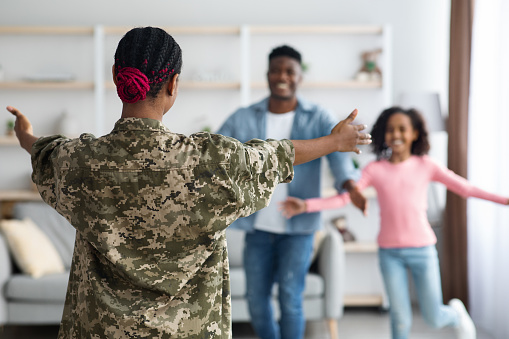 Happy black girl teenager and man running towards woman in military uniform, back view of african american female soldier return home from army, family reunion at home, blurred background