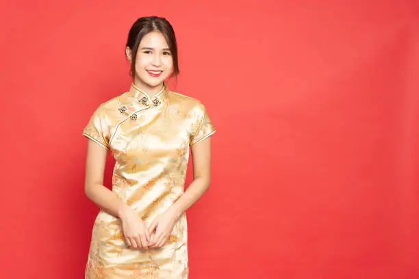 Young Asian woman wearing golden traditional cheongsam qipao dress isolated on red background, Happy Chinese New Year concept
