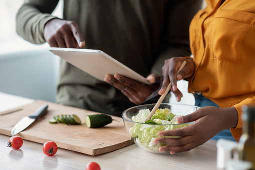 Black Couple Checking Recipe In Digital Tablet While Cooking Together In Kitchen, Cropped Shot Of Young African American Spouses Using Modern Gadget While Preparing Lunch At Home, Closeup
