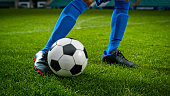 Close-up of a Leg in a Boot Kicking Football Ball. Professional Soccer Player Hits with Fierce Power, Scores Goal, Grass Flying. Football Championship Concept. Low Angle Ground Artistic Shot.