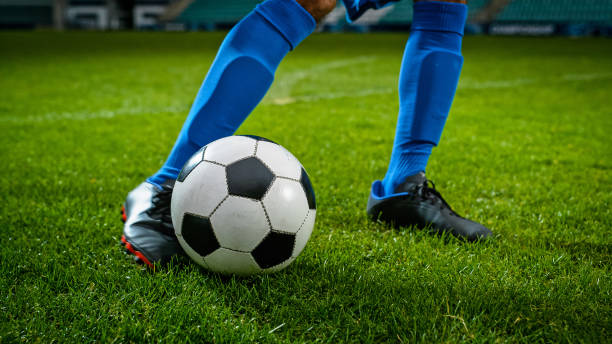 Close-up of a Leg in a Boot Kicking Football Ball. Professional Soccer Player Hits with Fierce Power, Scores Goal, Grass Flying. Football Championship Concept. Low Angle Ground Artistic Shot. stock photo