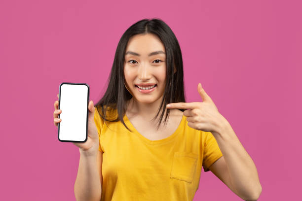istock Check this out. Excited korean lady pointing at smartphone with empty screen on violet background, mockup 1480040369