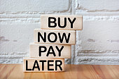 Against the background of a white brick wall, wooden blocks with the text BUY NOW, PAY LATER.