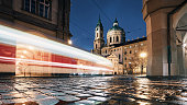 Light trail of tram passing between historical buildings at night