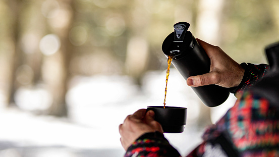 Close-up of man with thermos pouring coffee, Close-up of man drinking coffee in winter forest, Fross with hot drink, winter camper drinking hot coffee from his thermos in snowy weather