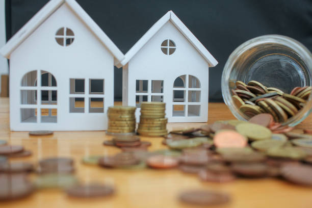monedas de euro apiladas frente a pequeñas casas - costes fotografías e imágenes de stock