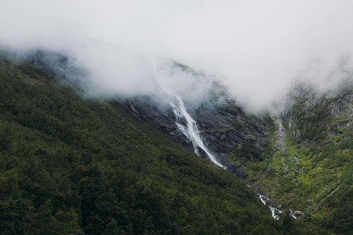 Low-angle view of the beautiful powerful waterfall hidden in the mountains during summertime in Scandinavia