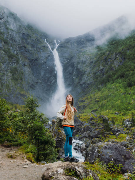 Handsome female explorer with long hair walking to dramatic Mardalsfossen waterfall hidden in the beautiful green mountain valley in Scandinavia