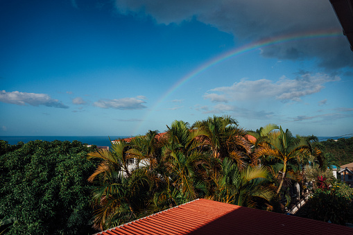 View from a balcony, looking out over the landscape to the Caribbean sea, with a rainbow arching over it.