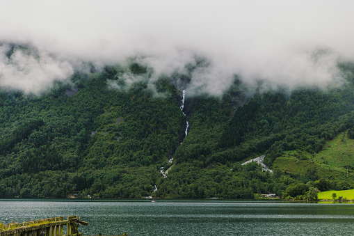 Scenic view of waterfront in morning mist with background view of green mountain and waterfall in Eidfjord, Scandinavia