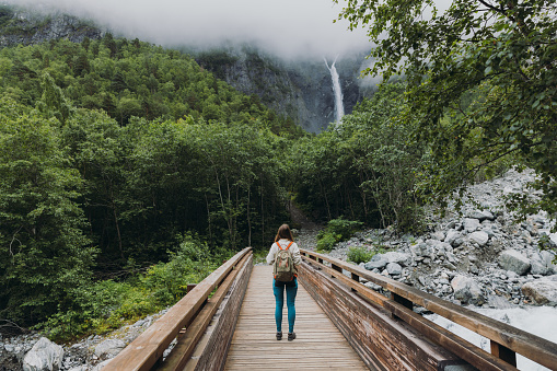 Happy woman backpacker walking to dramatic Mardalsfossen waterfall hidden in the summer green valley in Scandinavia