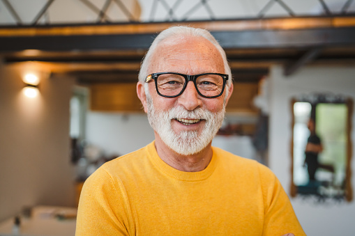 One modern senior caucasian man portrait of male grandfather with beard stand in his house in day wear yellow sweater happy confident copy space portrait