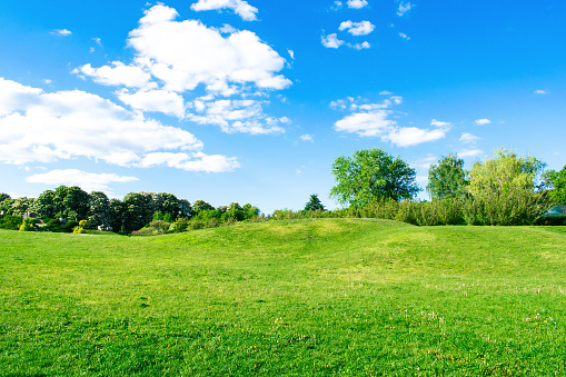 Scenic view of beautiful small mountains, hills, mounds with green grass lawn against bright blue sky with clouds in city park.