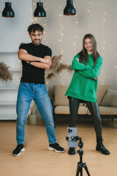 istock Cheerful man and woman dancing at camera filming video using phone on tripod at home, creating content on to share on social media. Blogger concept. New trends for millennial people concept 1480061690