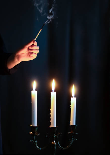 istock Hand igniting candles with match stick on the dark background. Condolence and mourning concept 1480062059