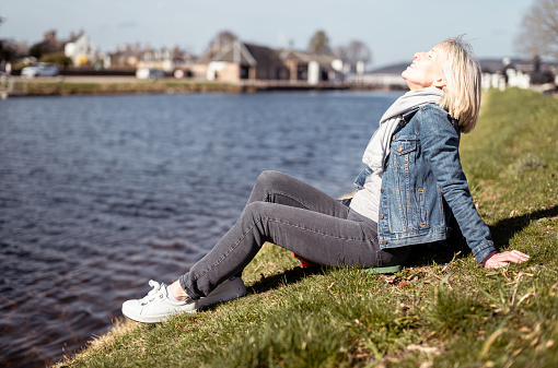 Mature woman sitting on the banks of the Caledonian Canal where it exits into the Moray Firth at Inverness, Scotland on a lovely Spring day.