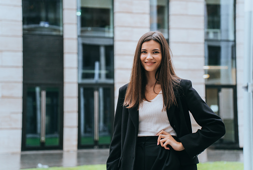 Young brunette businesswoman standing outside looks cat camera. Pretty Asian woman in black suit goes to office. Successful manager stands business center. Financial people. Lawyer goes to court.