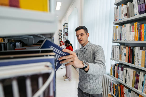 istock Male Student Picking Up A Book In A School Library 1480064038
