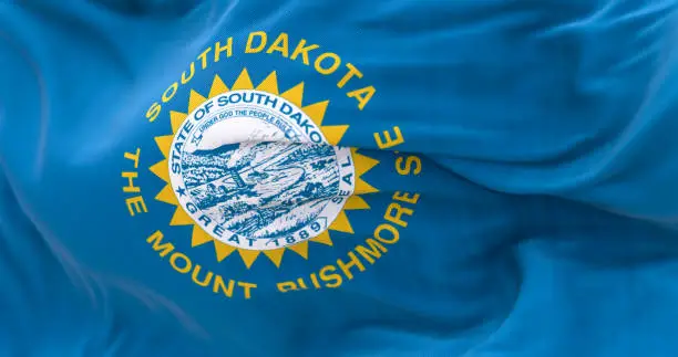 Close-up of South Dakota flag waving in the wind. Sky blue field with state seal and golden sun. US federate state. 3d illustration render. Selective focus. Close-up. Fluttering textile
