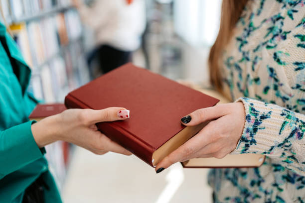 Two female students exchanging books in a student library in college. Close-up.