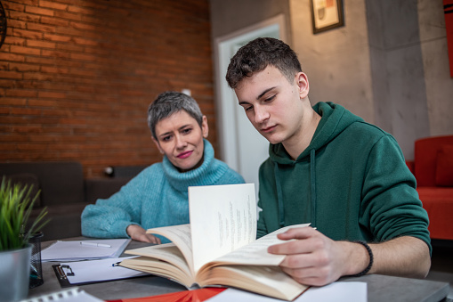 A teenage student studies with the help of one parent, the mother, who helps him solve assignments and prepare for the next exam at college or school