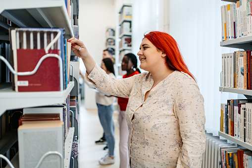 Beautiful young plus size woman picking up a book in a student library in college.