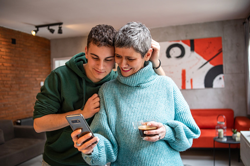 Mother and teenage son hugging, having fun and looking at mobile phone, taking selfie