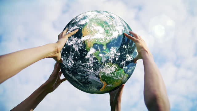 Multiple people holding a rotating planet Earth globe up in the air